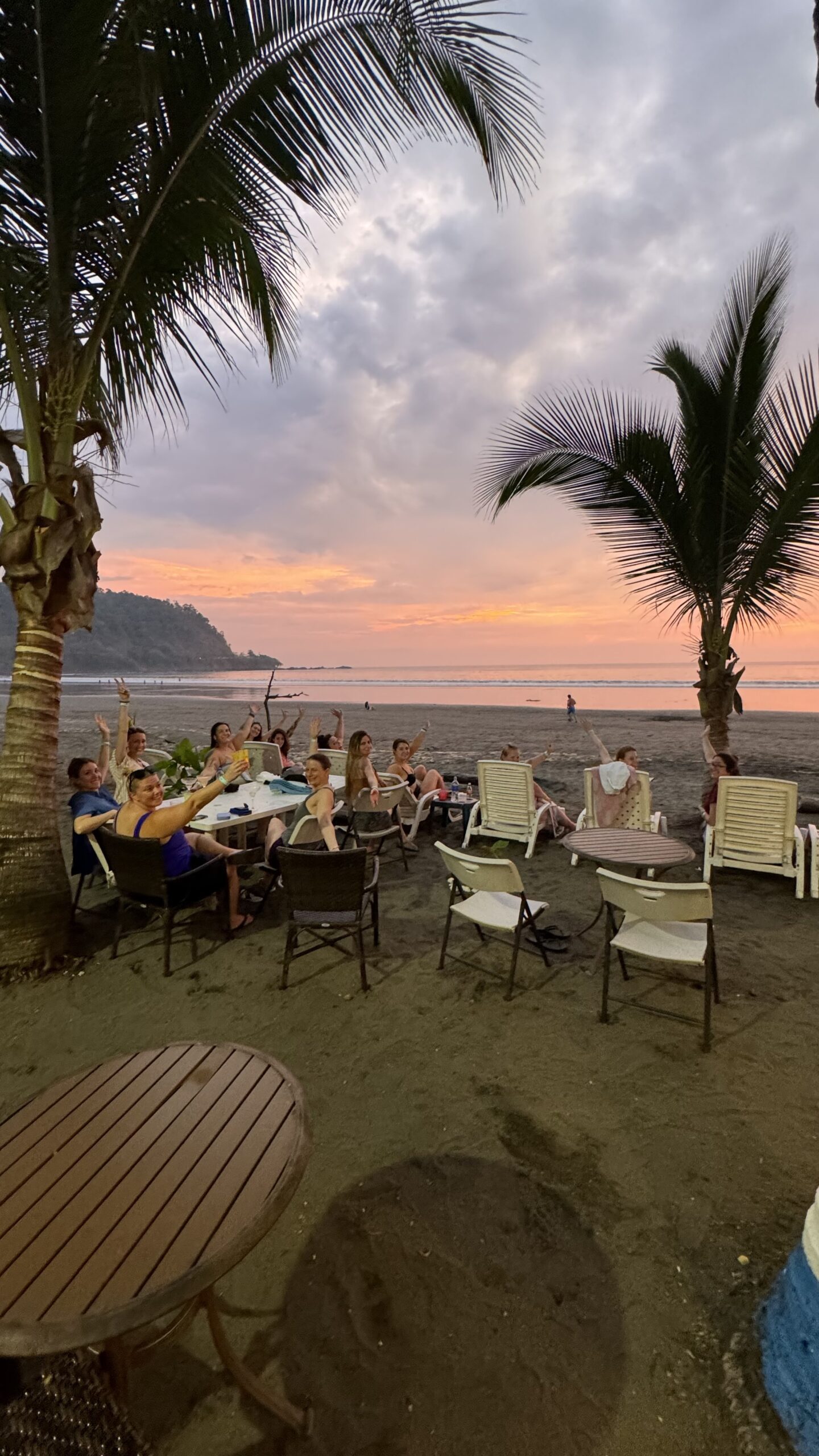 A large group of women seated beachside during a sunset.