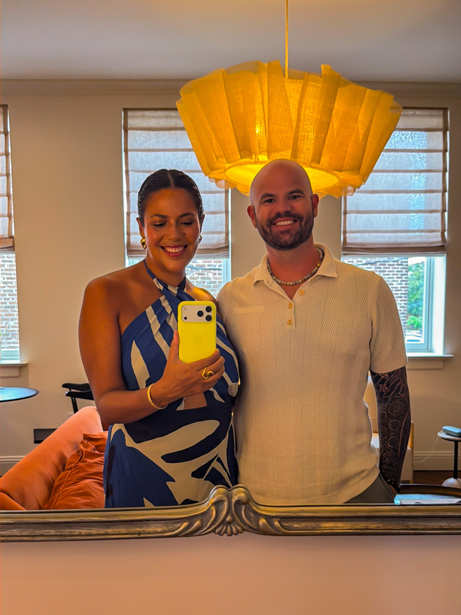 Ali and Skyline taking a mirror selfie under a pleated yellow pendant light in their suite at The Pinch