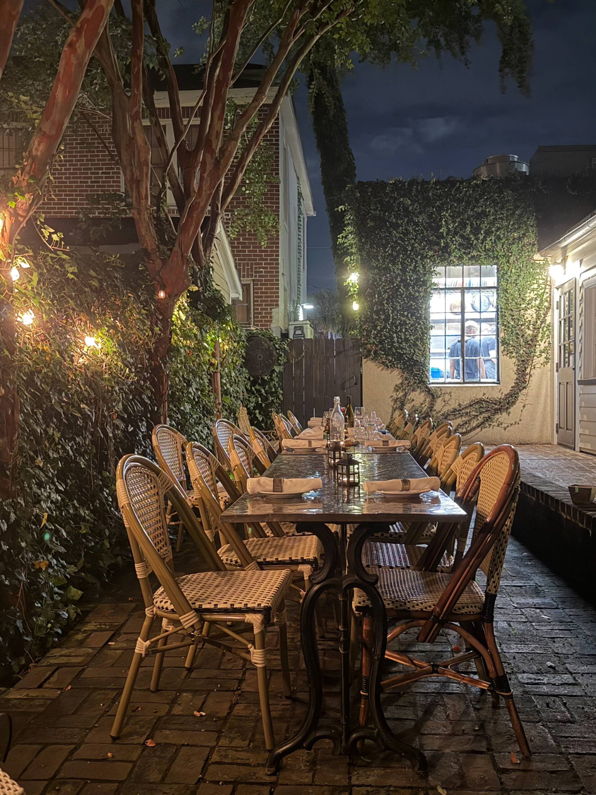 Long table set for dinner under string lights in the ivy-covered courtyard at Chez Nous in Charleston