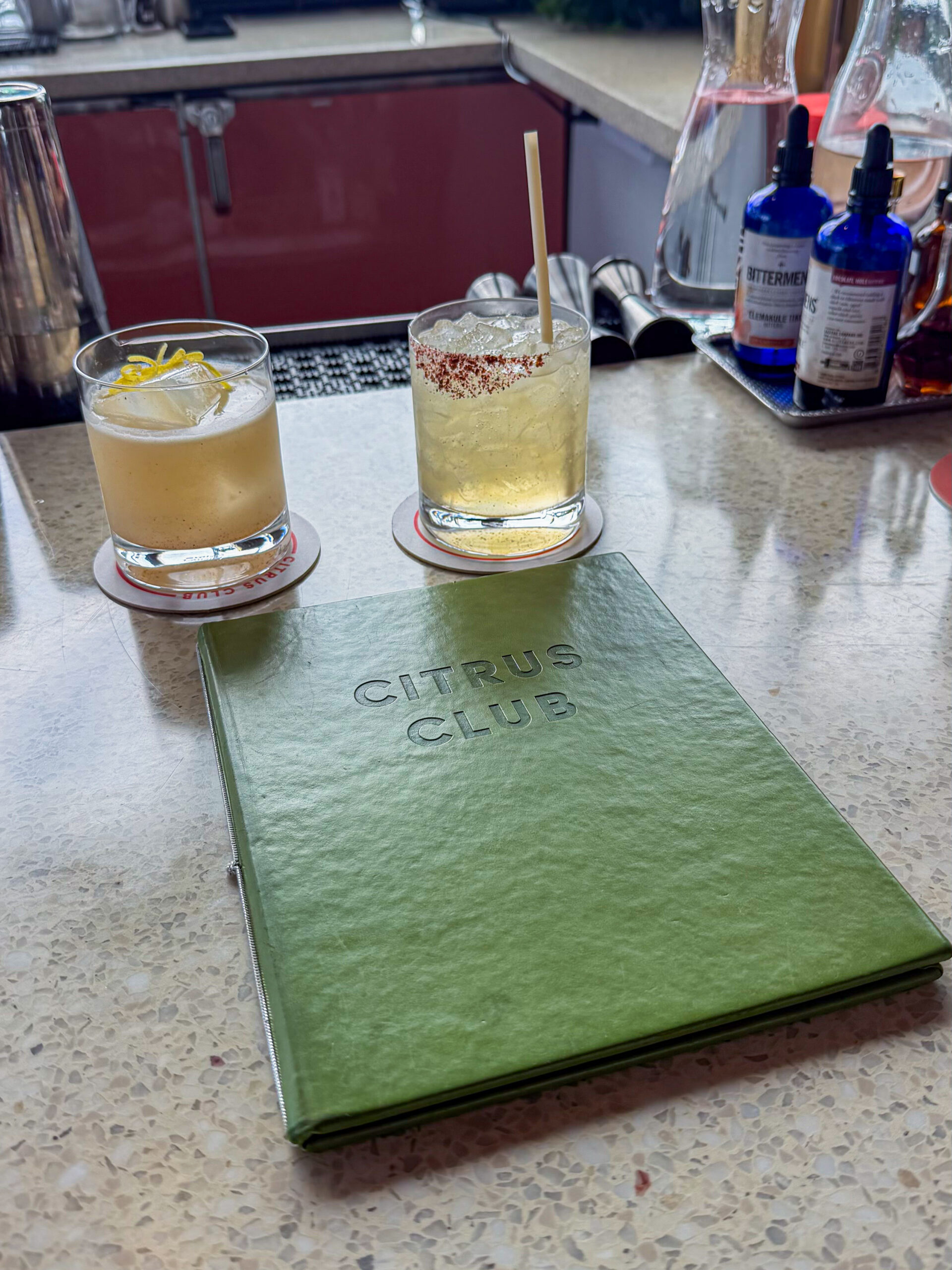 Two cocktails beside the green Citrus Club menu on the bar at The Dewberry in Charleston