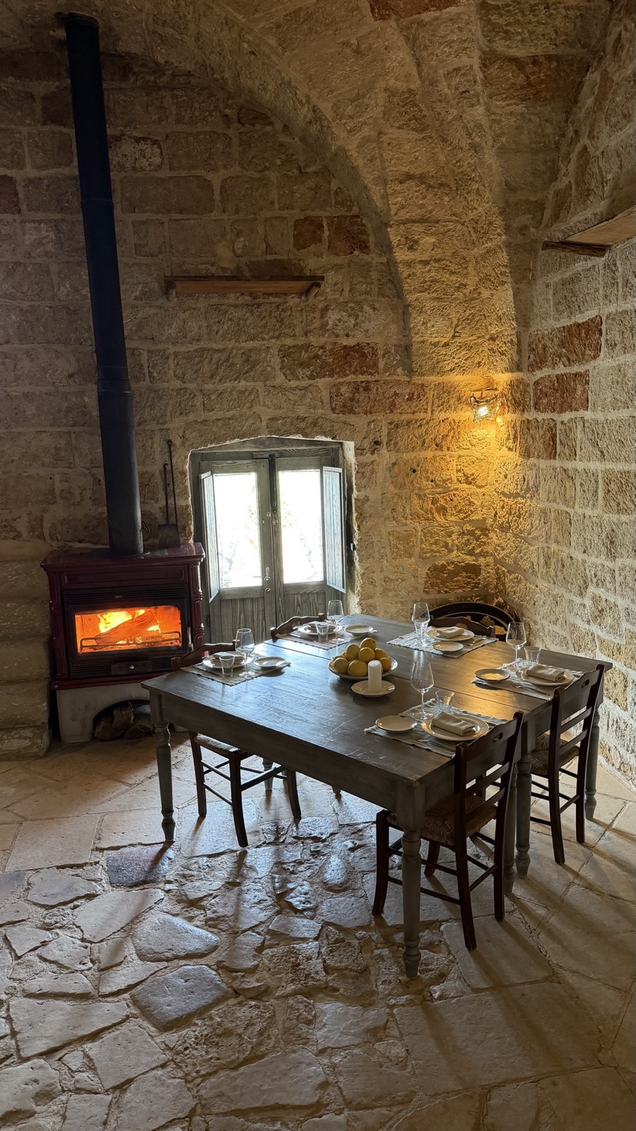 Vaulted stone dining room at Masseria Le Stanzie with a lit wood stove and a table set with lemons and a candle