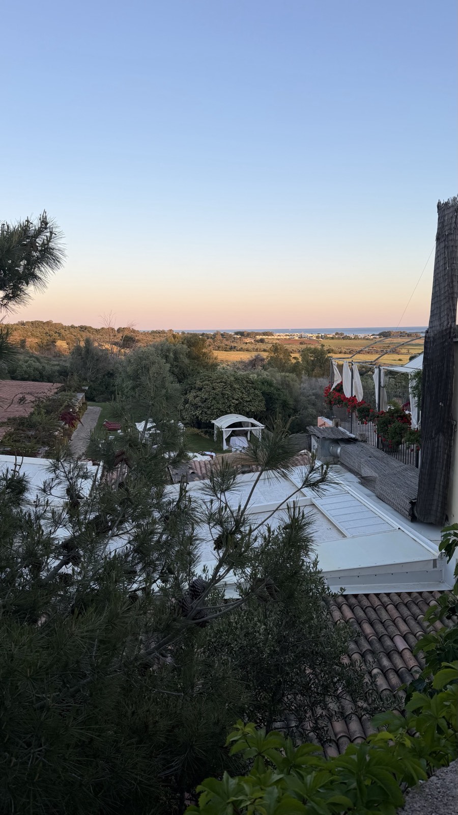 View from a masseria room over terracotta roofs and gardens out to fields and the sea at sunset in Salento